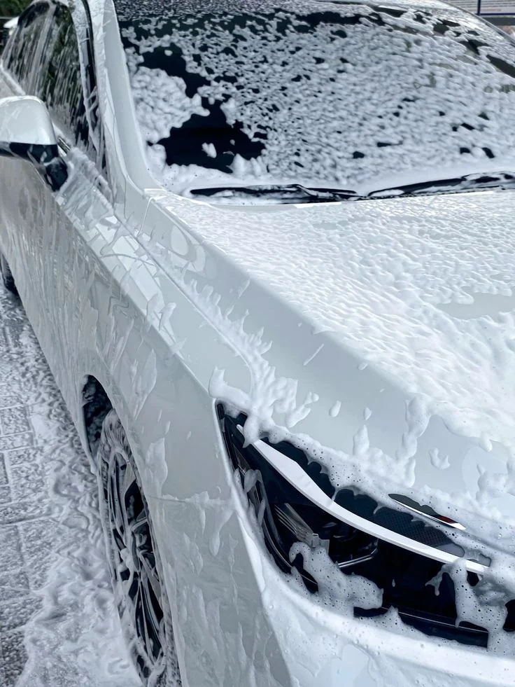 Auto blanco cubierto de espuma durante el lavado de la carrocería